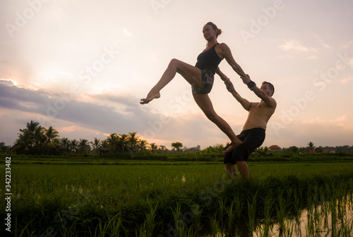 outdoors sunset acroyoga workout silhouette- young happy and fit couple practicing acro yoga drill at beautiful rice field enjoying nature and healthy lifestyle