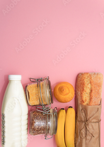 Donation food. Corn, buckwheat in jar, bananas, milk, bread, lemon, toilett paper on pink background. photo