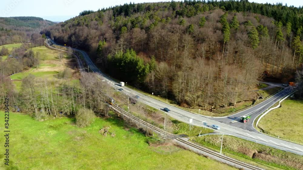 Black yellow short train travels in a lush green landscape in the black forest along curvy road with cars. Aerial drone tracking shot. Black yellow short train travels in a lush green landscape in the black forest along curvy road with cars. Aerial drone tracking shot.