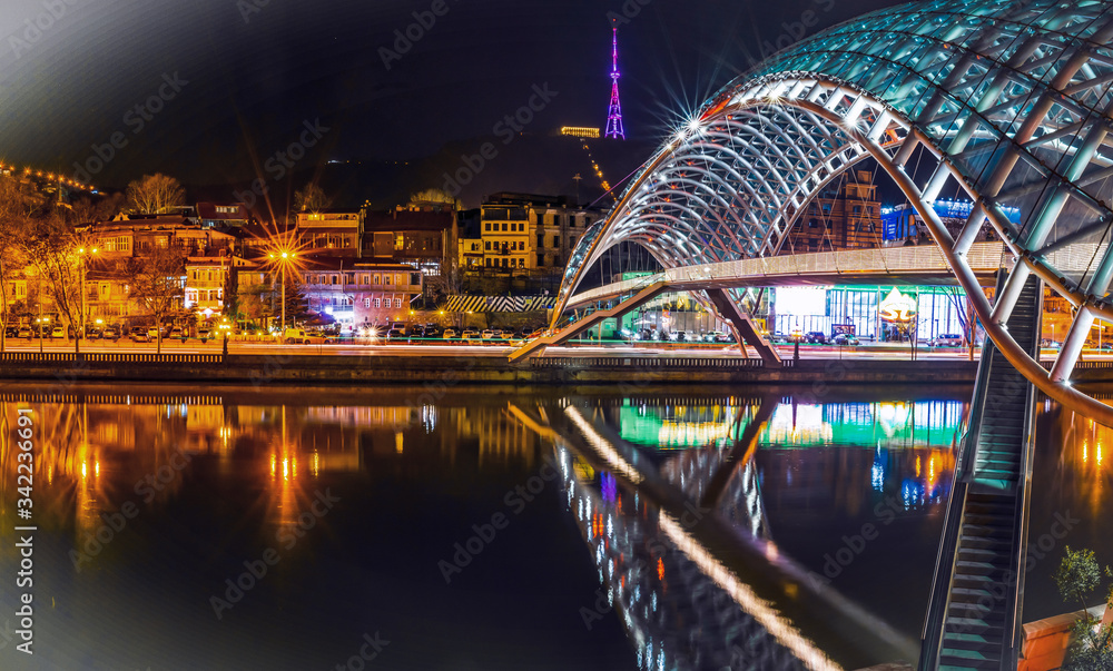 Obraz premium Side night view of illiuminated the bridge of peace and old town in the background. Sighseeing objects and architecture in Tbilisi.Georgia.2020