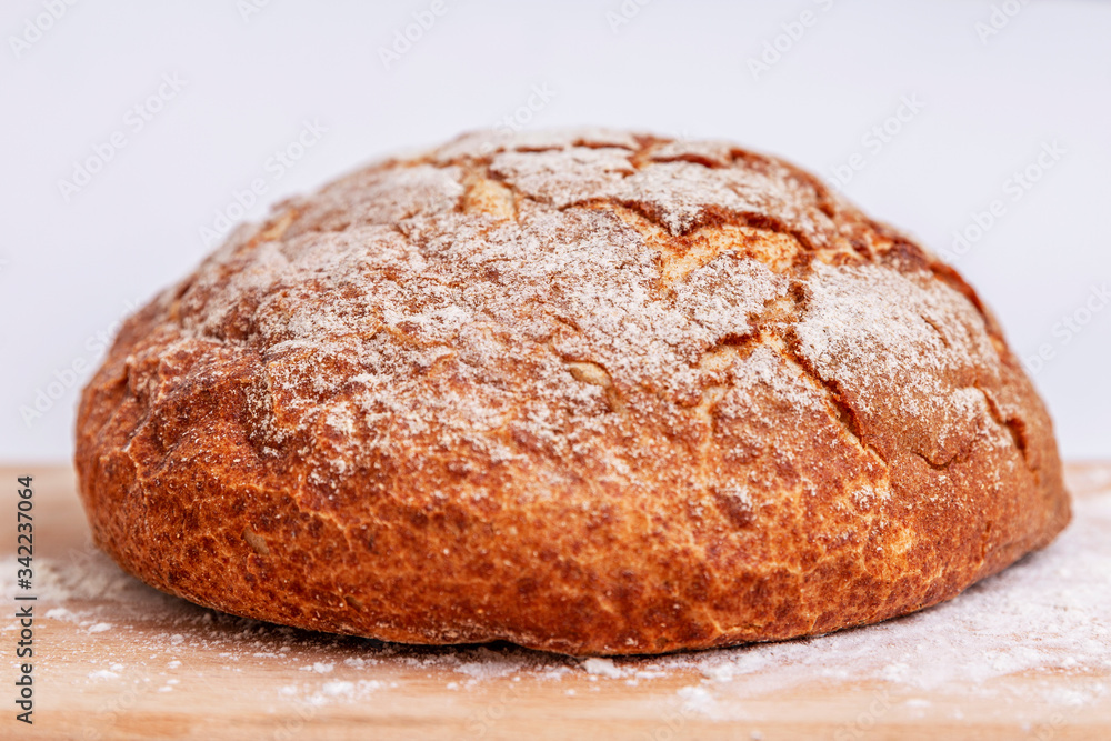 A leavened brown self-made bread covered in flour on a table. On a white background.