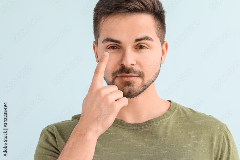 Young man with contact lens on color background Young man with contact lens on color background