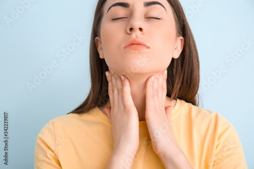 Young woman checking thyroid gland on color background