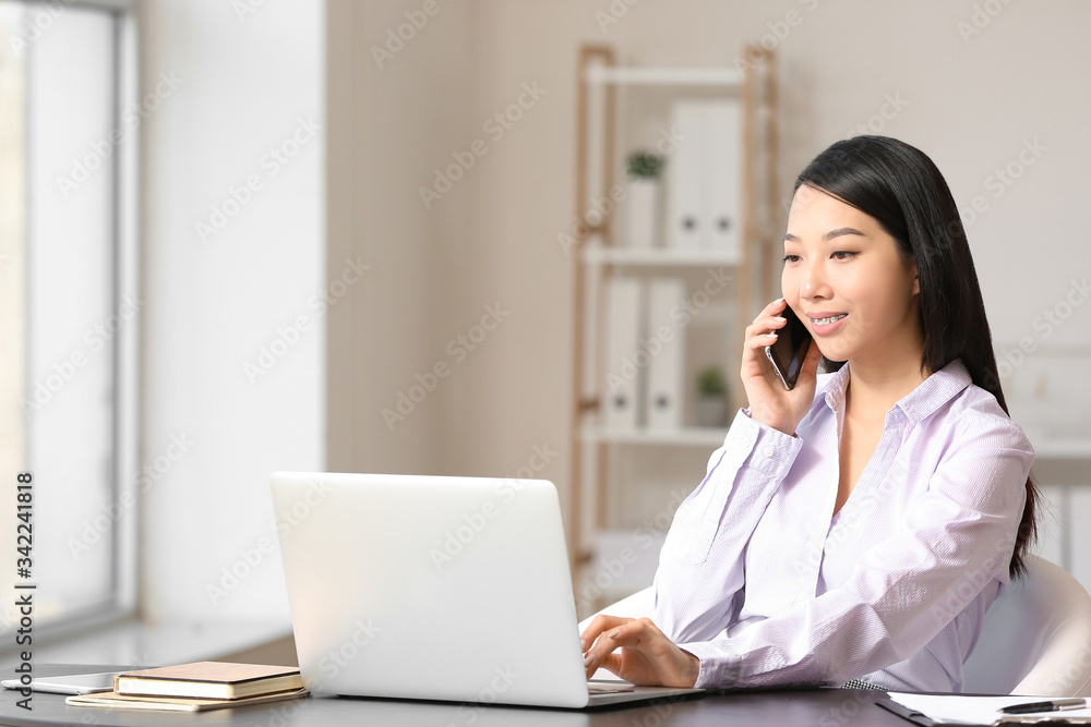Portrait of young Asian businesswoman talking by phone at table in office Portrait of young Asian businesswoman talking by phone at table in office