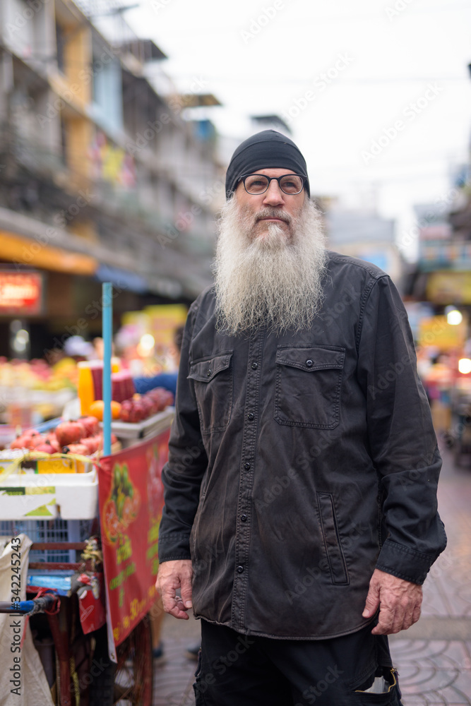 Mature bearded tourist man with eyeglasses thinking in Chinatown