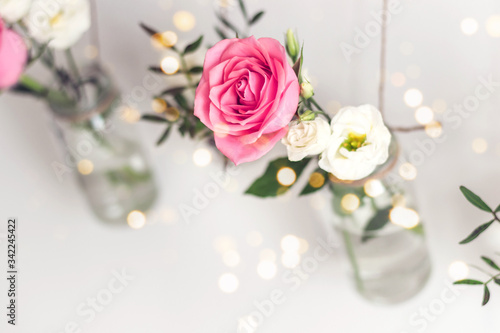Beautiful stylish holiday decoration. Roses in vases jars are suspended from white wall. Seasonal romantic decoration, selective focus