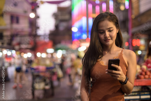Young beautiful Asian tourist woman using phone in Chinatown at night