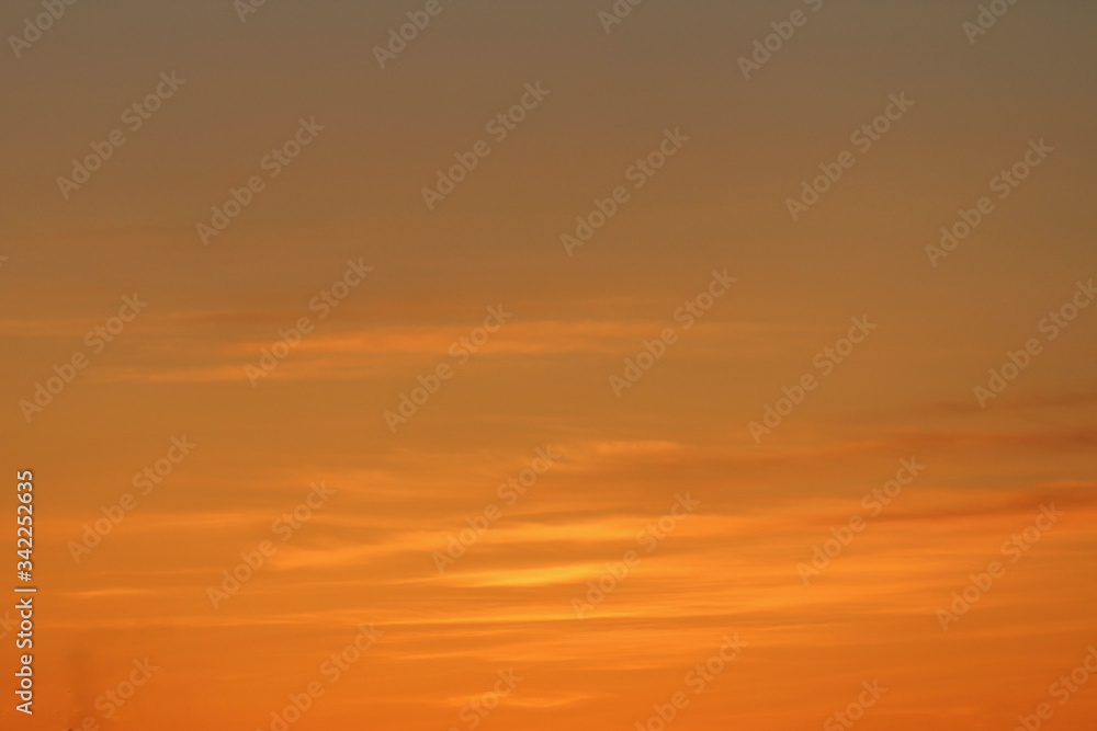 Sun below the horizon and clouds in the fiery dramatic orange sky at sunset or dawn backlit by the sun. Place for text and design.