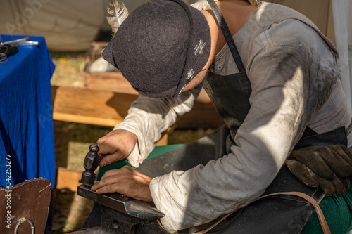 Hands of the master. Shapes the metal by striking the anvil with a hammer. Old crafts.  Conducts a master class. Workshop. Dressed in an old outfit.  Demonstration of the craft.