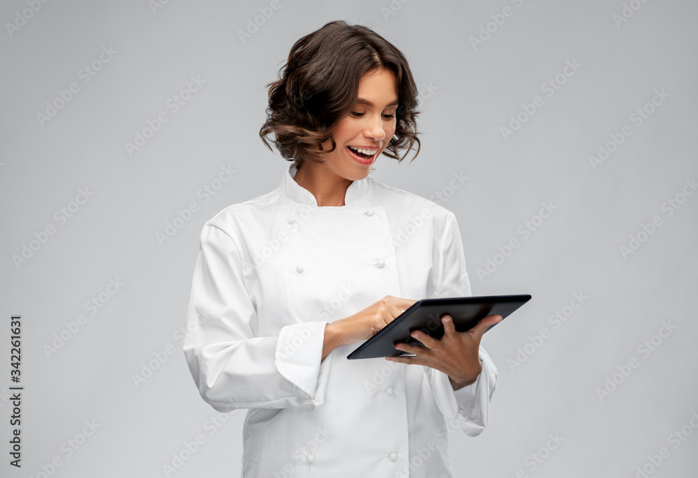 cooking, culinary and people concept - happy smiling female chef in toque with tablet pc computer over grey background cooking, culinary and people concept - happy smiling female chef in toque with tablet pc computer over grey background