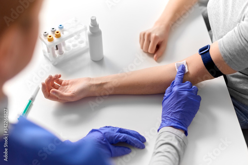 medicine, healthcare and diabetes concept - close up of doctor in gloves disinfecting patient's hand with wound wipe after taking blood for test at hospital © Syda Productions