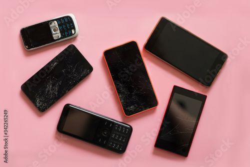 various types of old  broken and modern  smartphones on pink background, top view