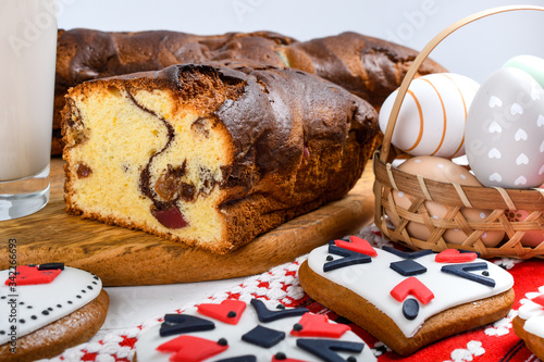 Slices of Romanian sponge cake or chec, cozonac with red traditional towel with manual stitch on wooden board, Easter painted eggs and home made ginger bread hearts, Authentic Easter Brunch concept.  photo