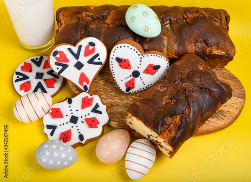 Slices of Romanian sponge cake or chec, cozonac with red traditional towel with manual stitch on wooden board, Easter painted eggs and home made ginger bread hearts, Authentic Easter Brunch concept.  photo