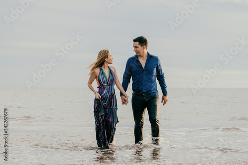 good looking couple looking each other straight in the eye, walking out of the ocean holding hands