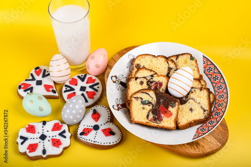 Slices of Romanian sponge cake or chec, cozonac with red traditional towel with manual stitch on wooden board, Easter painted eggs and home made ginger bread hearts, Authentic Easter Brunch concept.  photo