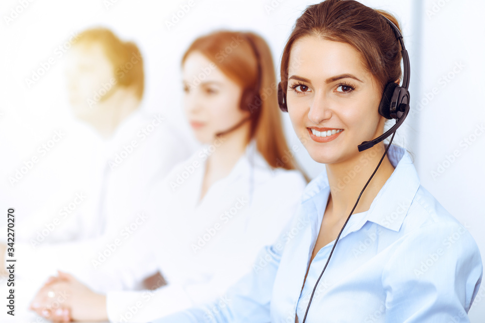 Call center operators. Focus on beautiful business woman using headset in sunny office Call center operators. Focus on beautiful business woman using headset in sunny office