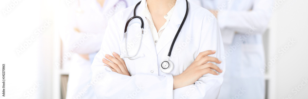 Unknown woman-doctor standing straight with arms crossed in clinic, close-up. Medical team ready to stop coronavirus pandemic. Medicine concept Unknown woman-doctor standing straight with arms crossed in clinic, close-up. Medical team ready to stop coronavirus pandemic. Medicine concept