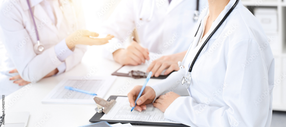 Group of unknown doctors discussing problems to stop coronavirus pandemic while sitting at meeting in clinic, close-up . Medicine concept Group of unknown doctors discussing problems to stop coronavirus pandemic while sitting at meeting in clinic, close-up . Medicine concept