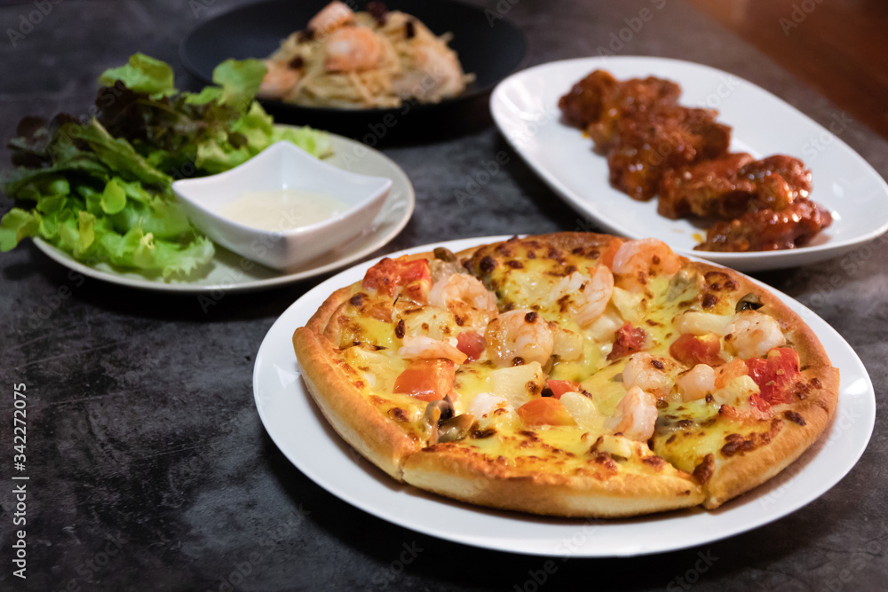 Pizza seafood with prawn and tomato, deep fried chicken wing with spicy sauce in Korean style, salad and spaghetti on table. 