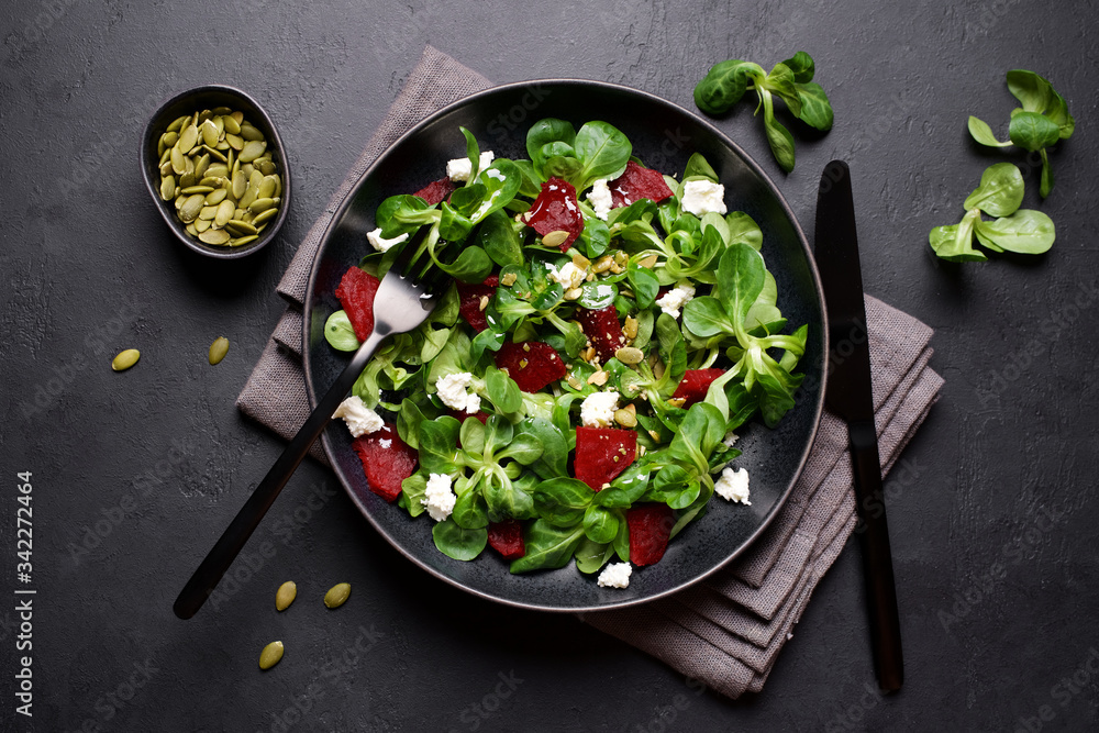 Corn salad with beets, cheese and pumpkin seeds. Dark background, top view. Corn salad with beets, cheese and pumpkin seeds. Dark background, top view.