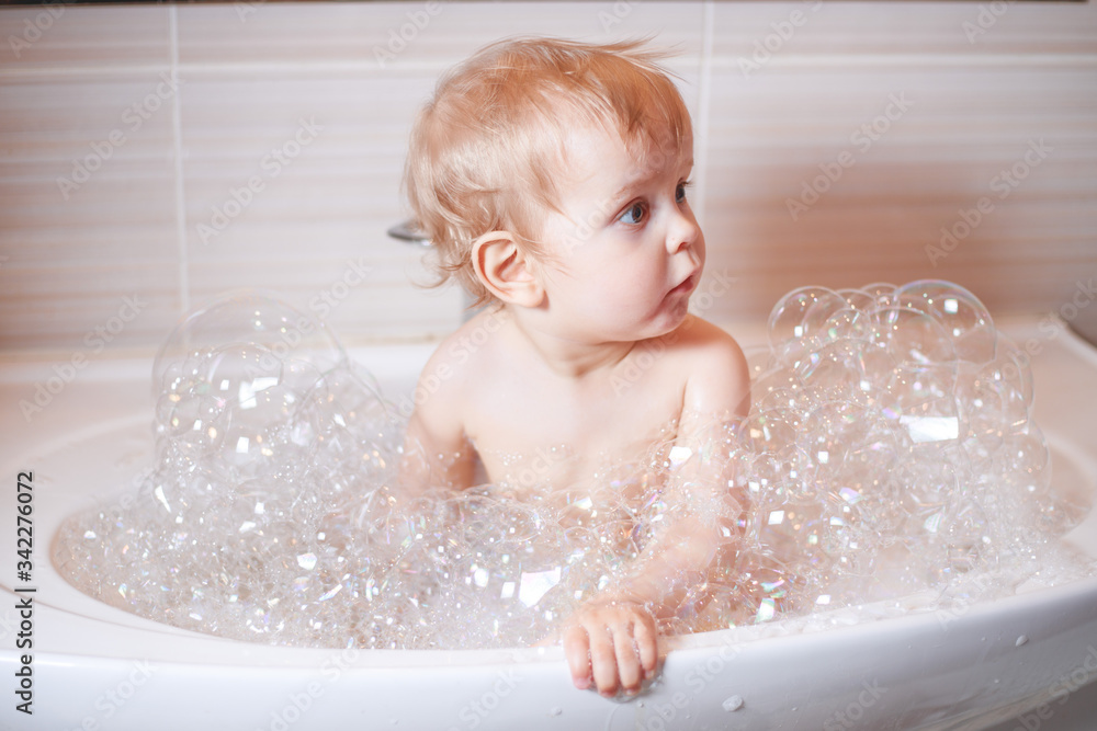 Happy laughing Infant baby toddler taking a bath playing with foam bubbles. Children care and hygiene concept. Happy laughing Infant baby toddler taking a bath playing with foam bubbles. Children care and hygiene concept.