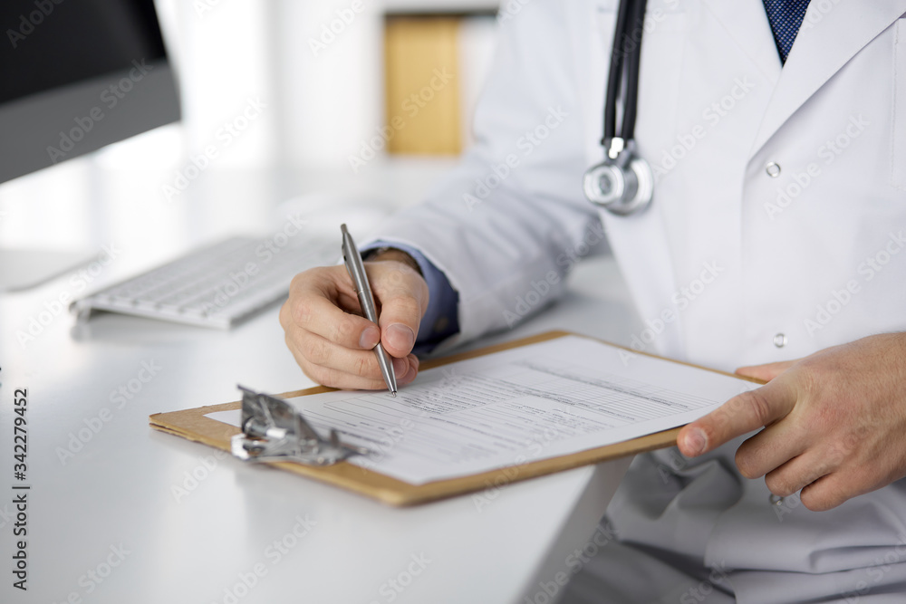 Friendly red-bearded doctor sitting and writing with clipboard in clinic, close-up Medicine concept Friendly red-bearded doctor sitting and writing with clipboard in clinic, close-up Medicine concept