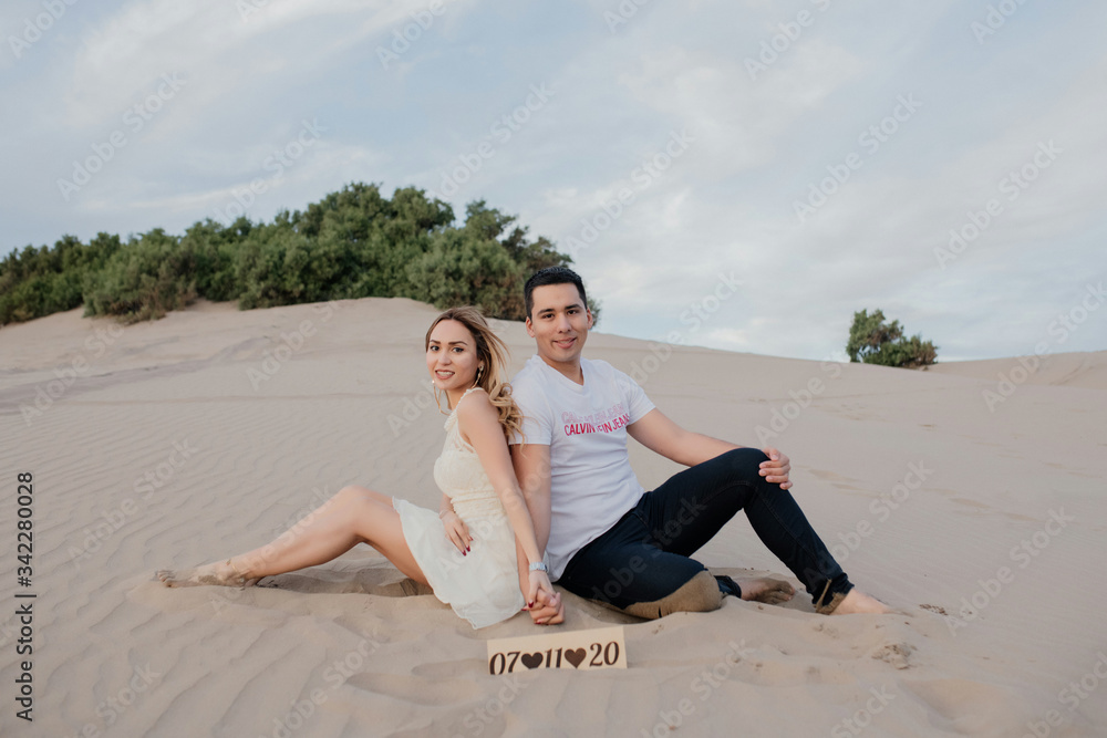 Φωτογραφία funny couple sitting on the sand holding hands
young couple wearing white 
beaut