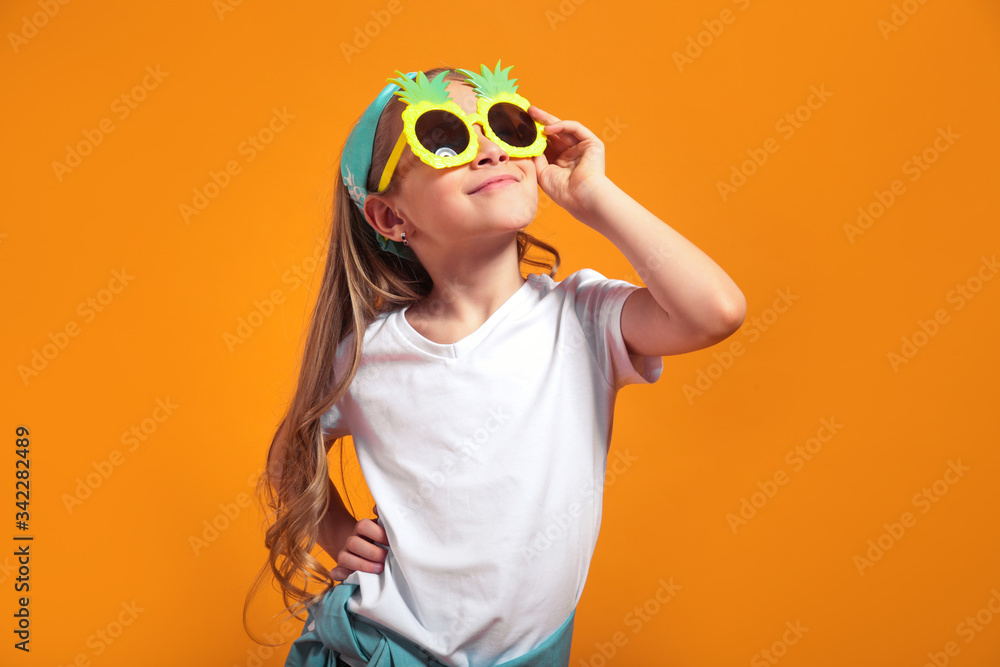 Smiling girl posing in the funny sunglasses and looking away on yellow background