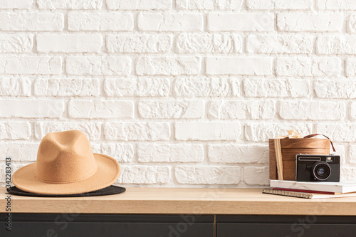 wooden shelf with retro photo camera and hat. Stylish interior of living room with white brick wall, brown box, elegant accessories. Minimalistic concept of home decor. Template.