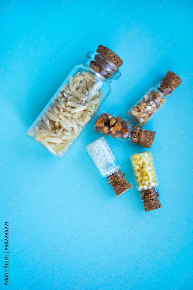 Vertical picture with soft focus of five tiny glass jar with rice, buckwheat, millet, sugar and barley on blue background, top view. Concept of nutrition, vegetarian products. Space for text Vertical picture with soft focus of five tiny glass jar with rice, buckwheat, millet, sugar and barley on blue background, top view. Concept of nutrition, vegetarian products. Space for text