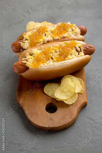 Homemade colombian hot dogs with pineapple sauce, chips and mayo ketchup on a rustic wooden board on a gray background, low angle view. Close-up.