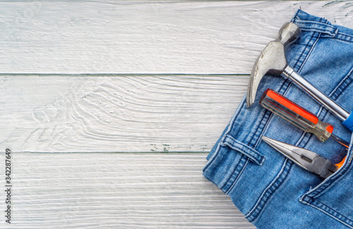 Jeans, screwdriver, hammer and pliers on wooden background. Jeans texture, Blue denim jeans with tools photo