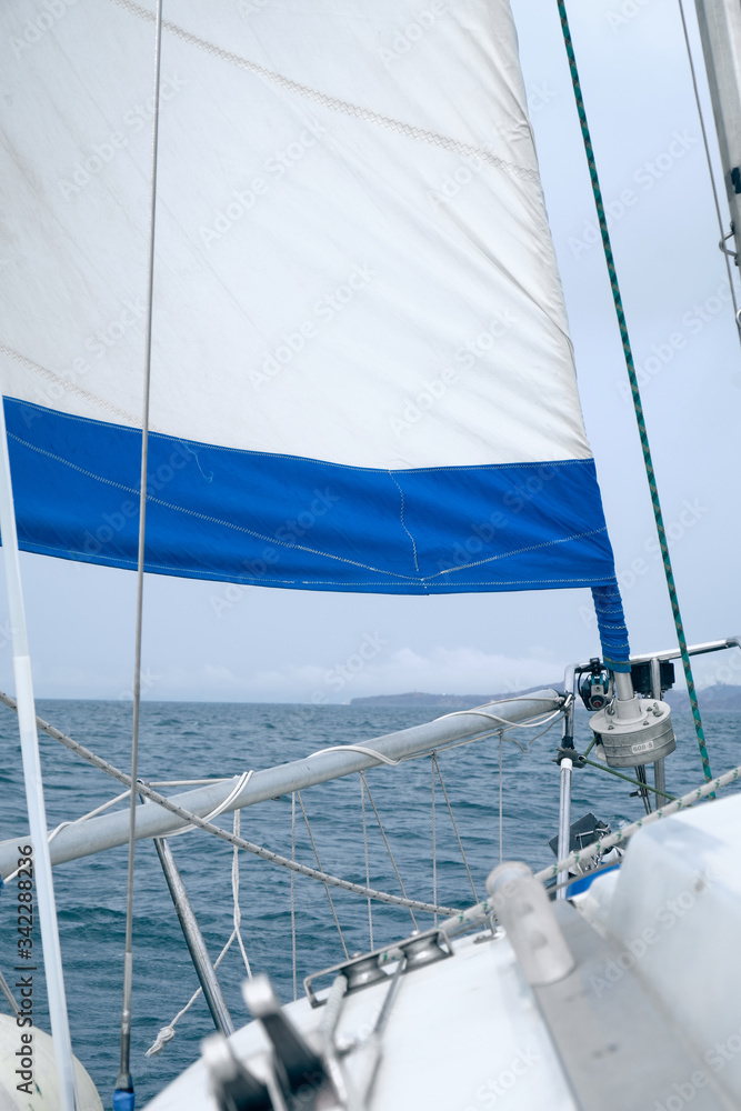 Fototapeta premium Cruising yacht bow with hoisted sails. Sailing at summer foggy day. Yachting concept and sea background