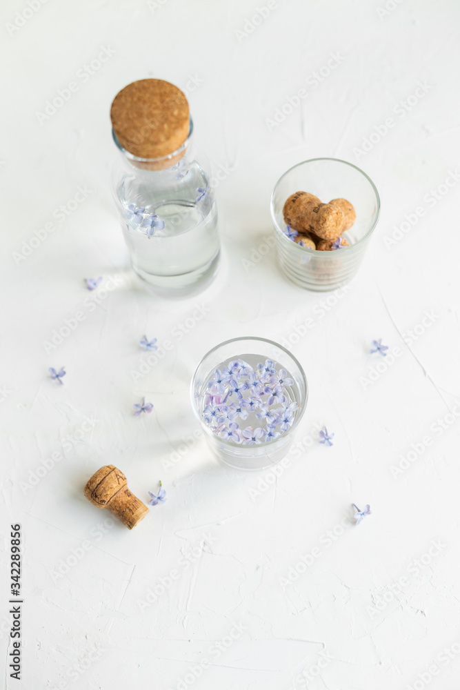 A glass of lilac water on the white table. Fresh spring flowers and pure water, healthcare concept. A glass of lilac water on the white table. Fresh spring flowers and pure water, healthcare concept.