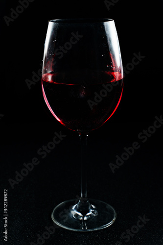 Transparent glass glass with a red alcoholic drink. Red wine in a glass on a black background