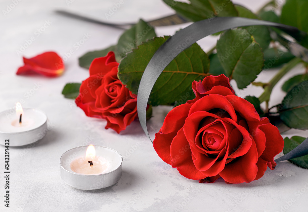 The concept of death and sorrow. Bouquet of fresh red roses next to two mourning candles on a white background The concept of death and sorrow. Bouquet of fresh red roses next to two mourning candles on a white background