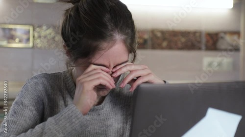 Girl close and rubs her dry eyes after working on laptop