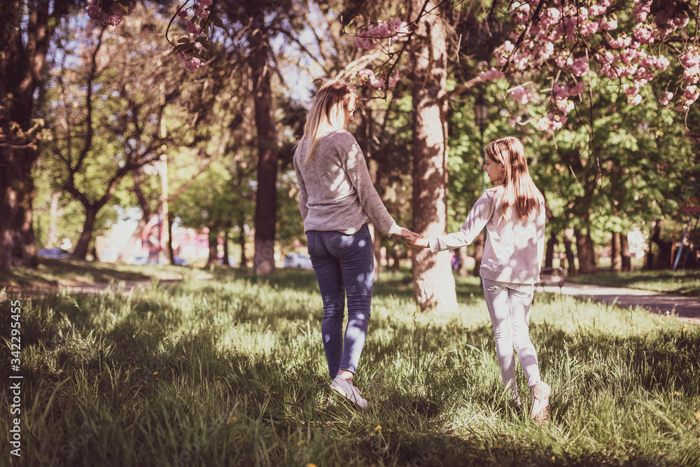 Obraz premium Sakura blossomed. Young mother with her child have fun in the park near the sakura. Spring morning. They look at each other