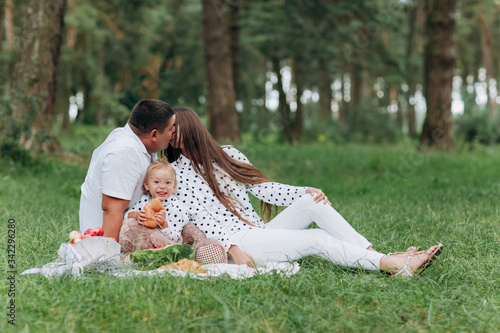 Mom, dad and daughter sitting on the picnic in the park, forest. The concept of summer holiday. Father's, mother's, baby's day. Spending time together. Family look. Couple kissing