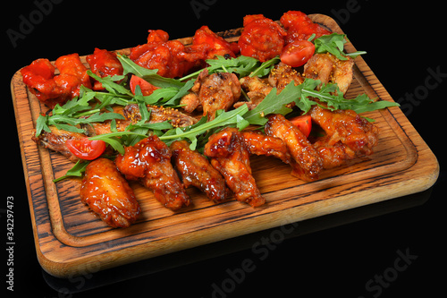 Baked chicken wings in spicy sauce, cherry tomatoes, arugula greens on a wooden Board
