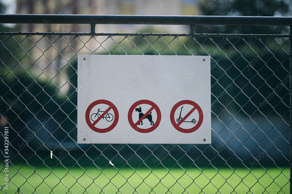 The sign on the fence with signs: dog walking is prohibited, riding a bicycle and scooter is prohibited. The sign on the fence with signs: dog walking is prohibited, riding a bicycle and scooter is prohibited.