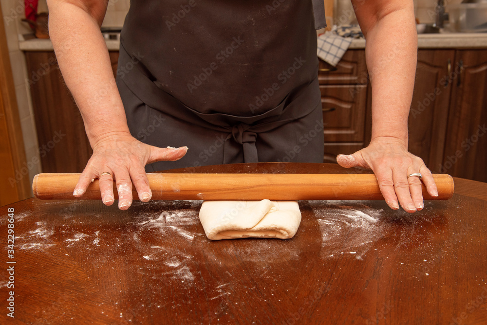 female hands roll out the pizza dough on a wooden table in the home kitchen. homemade food female hands roll out the pizza dough on a wooden table in the home kitchen. homemade food