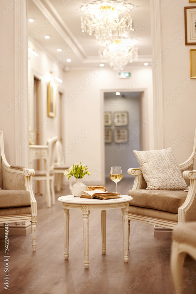 Fototapeta premium An open vintage book, a glass of white wine and crunchy pastries sit on a vintage table in the bright, cozy living room
