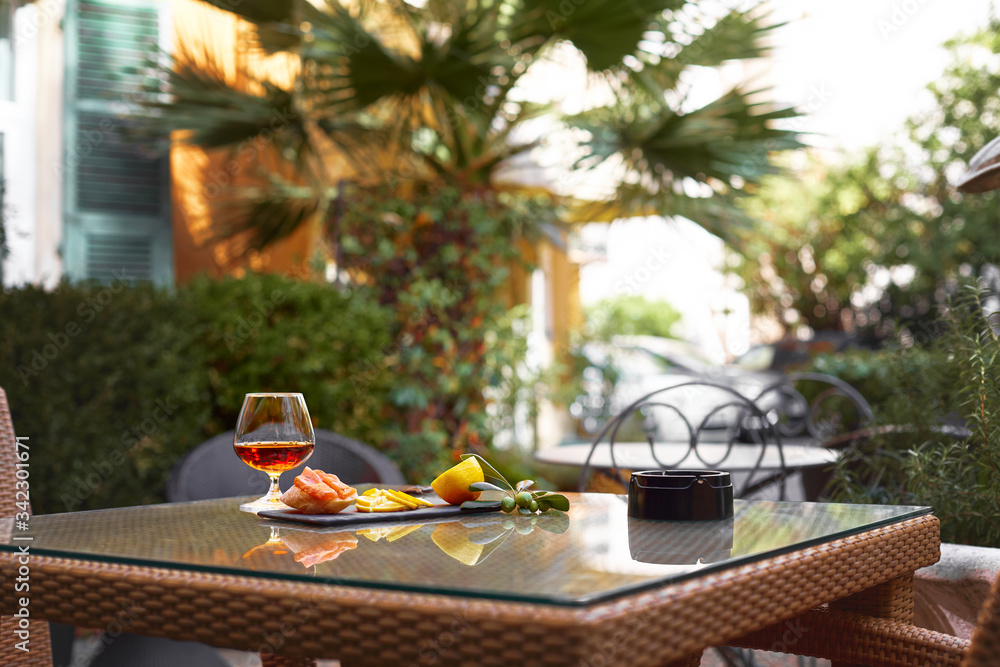A glass of cognac, slices of lemon, a sandwich and a sprig of olive lie on the table on the restaurant's terrace. Rest, relaxation