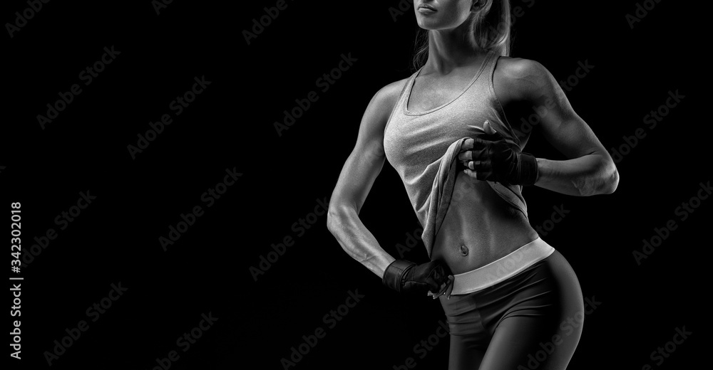 Fitness woman in sports tank top, gloves. Black and white close-up photo. Fitness athletic young woman showing her well trained body, six pack, perfect abs, shoulders, biceps, triceps and chest.