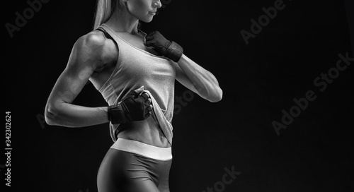 Cropped black and white shot of a strong woman with muscular abdomen in sportswear. Fitness female model on black background. Beautiful woman isolated on dark background.