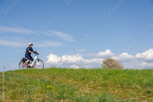 Frau fährt Fahrrad im Frühling über grüne Wiese vor blauem Himmel