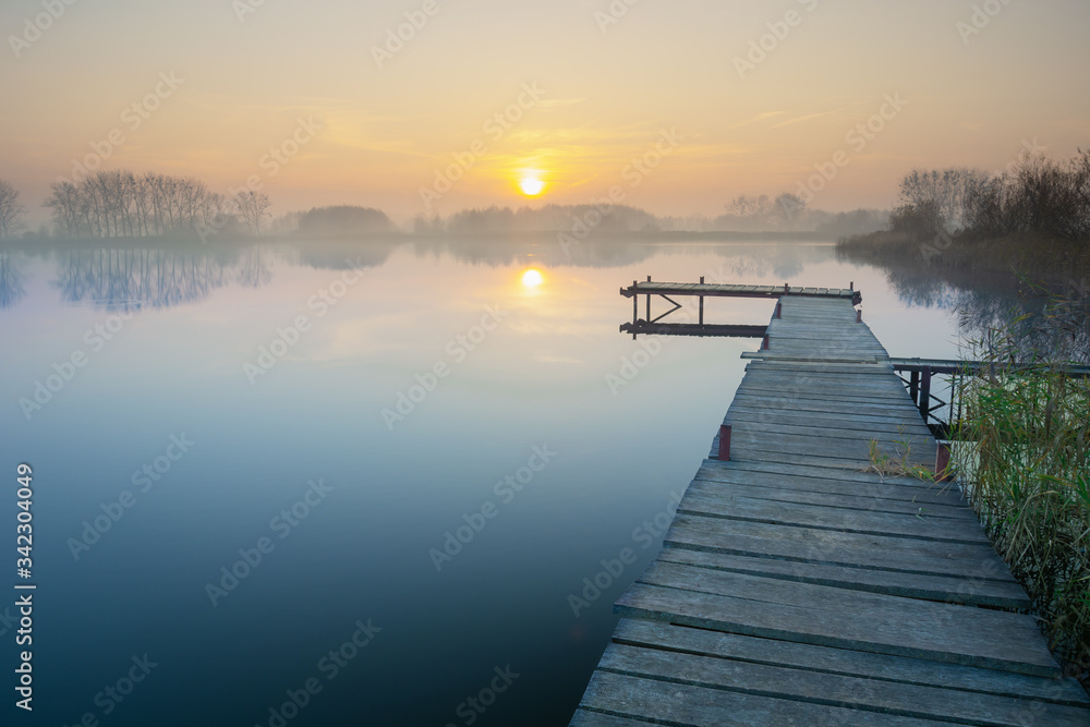 Wooden jetty on a calm and misty lake during sunset