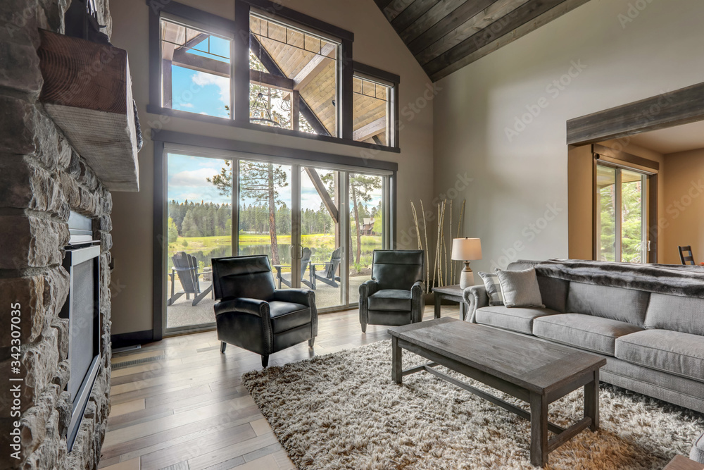 Living room luxury interior with large stone fireplace and leather furniture and huge tall windows with natural tones with TV. Living room luxury interior with large stone fireplace and leather furniture and huge tall windows with natural tones with TV.